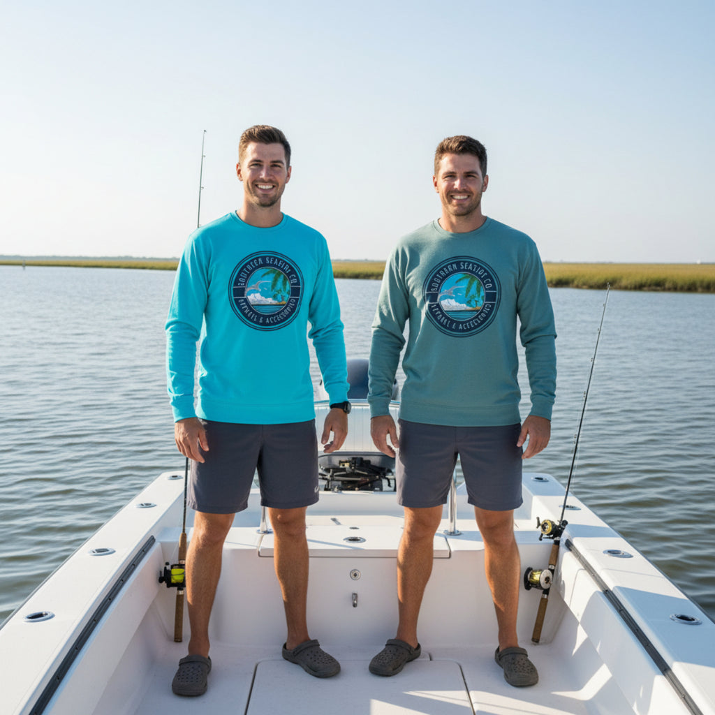 Two men on a boat wearing matching blue and green sweatshirts with a Southern Seaside logo, standing in front of a body of water.