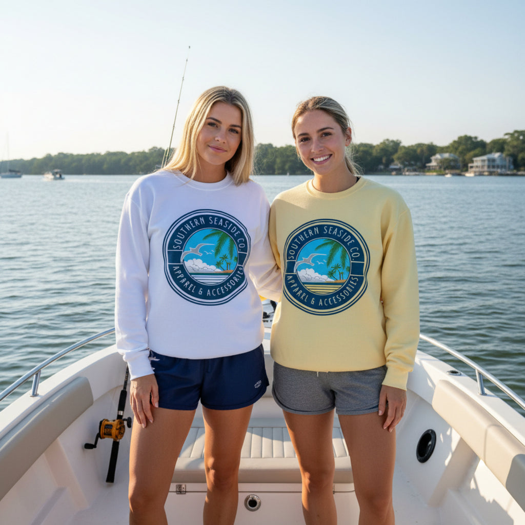 Two women on a boat wearing Comfort Colors sweatshirts with a Southern Seaside logo, smiling at the camera.