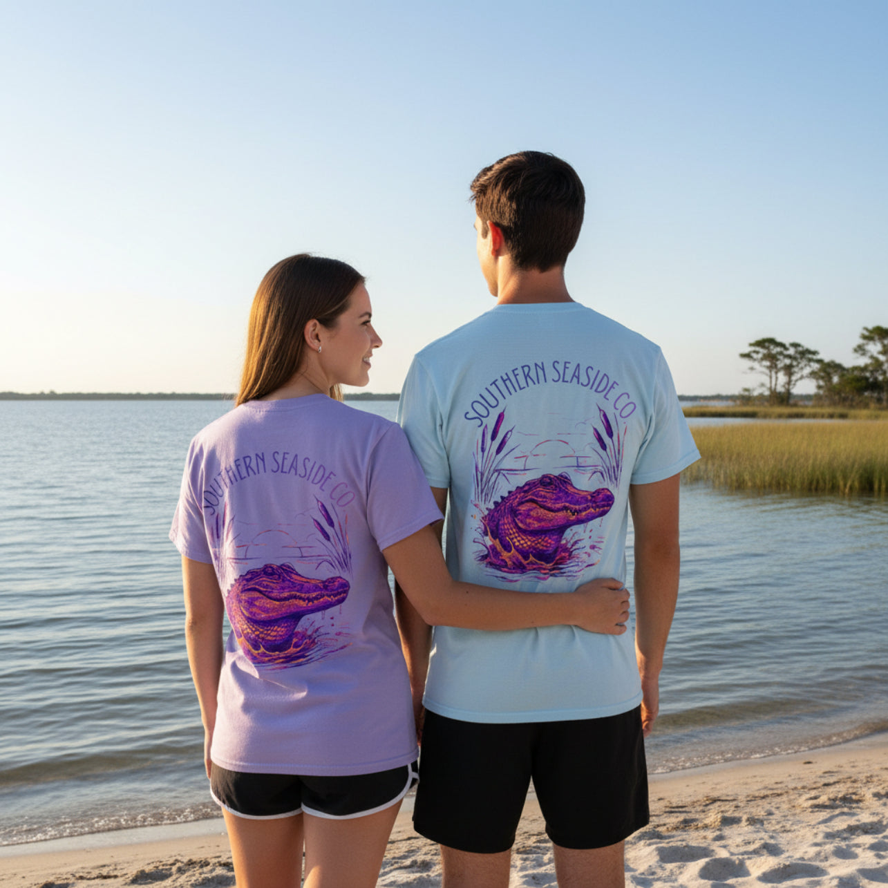 Two people standing on a beach wearing t-shirts with a purple alligator design and 'Southern Seaside Co.' text.