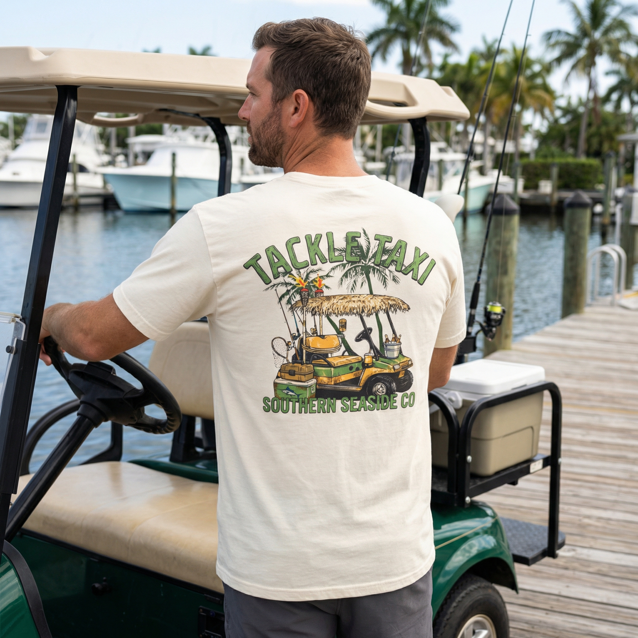 Man driving a golf cart wearing a 'Tackle Taxi' t-shirt by a marina. The tshirt is golf cart and fishing gear themed. 