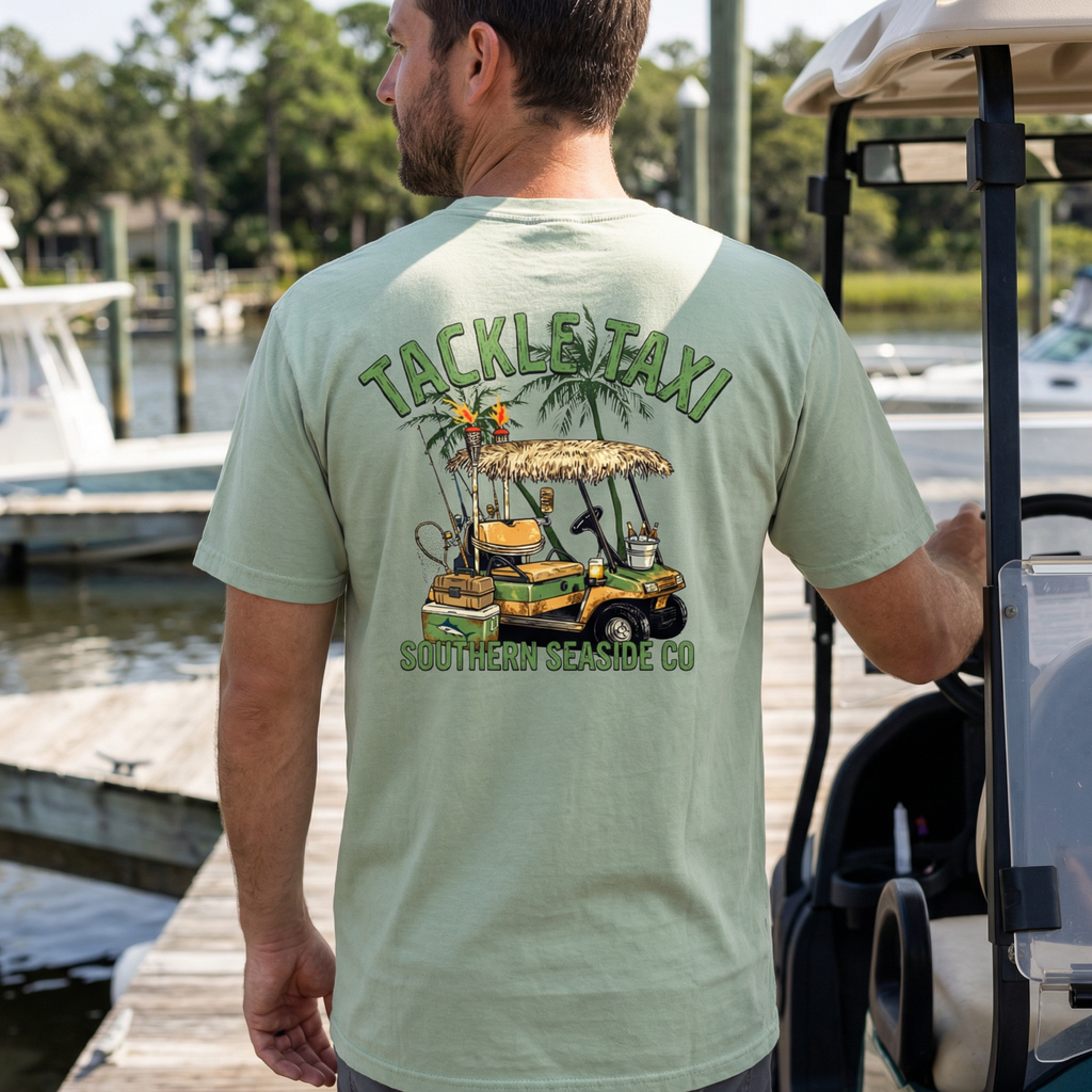 Man wearing a light green t-shirt with a golf cart and fishing gear with 'Tackle Taxi' design by Southern Seaside Co. at a dock.