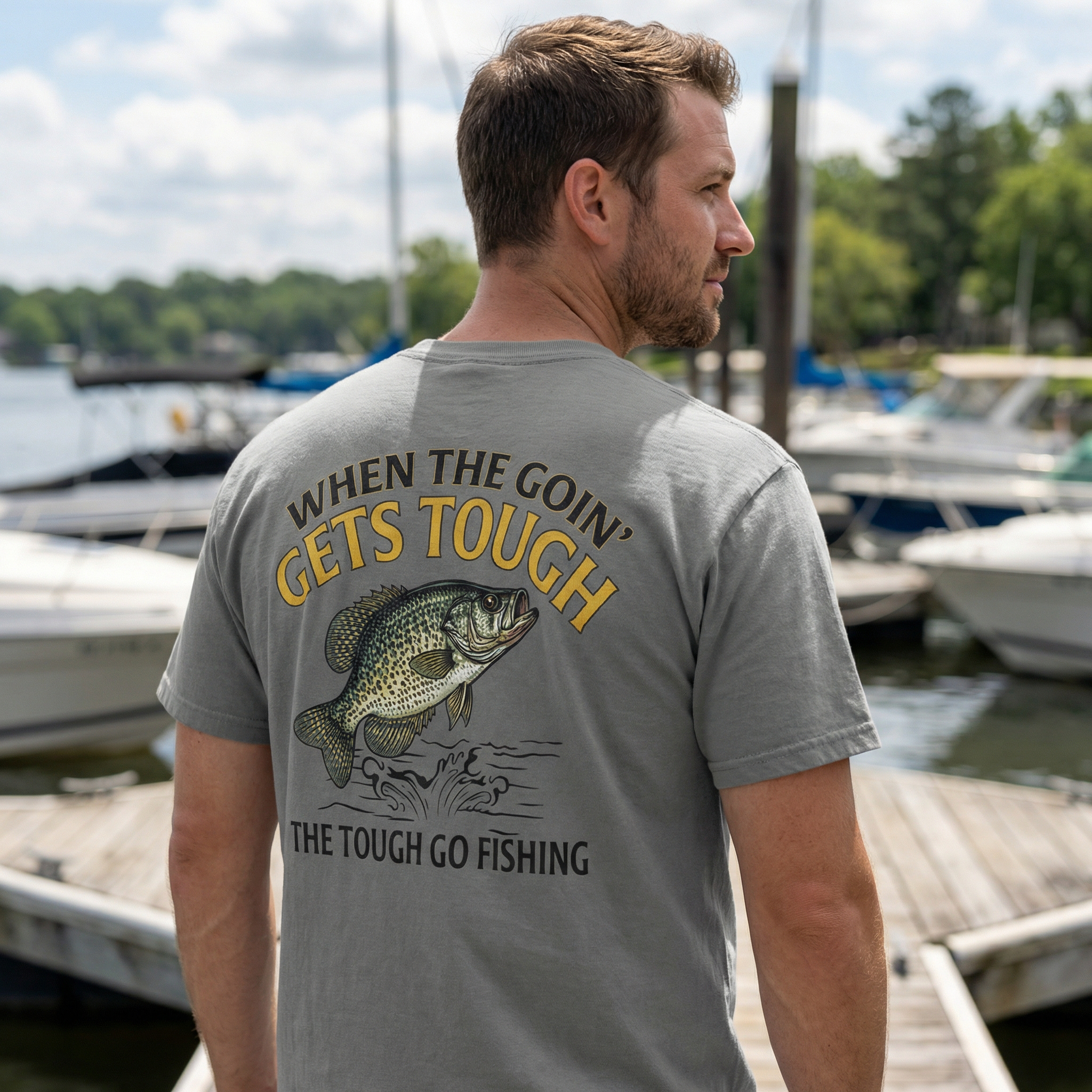 Man wearing a gray t-shirt with a crappie fishing-themed text and graphics at a marina.