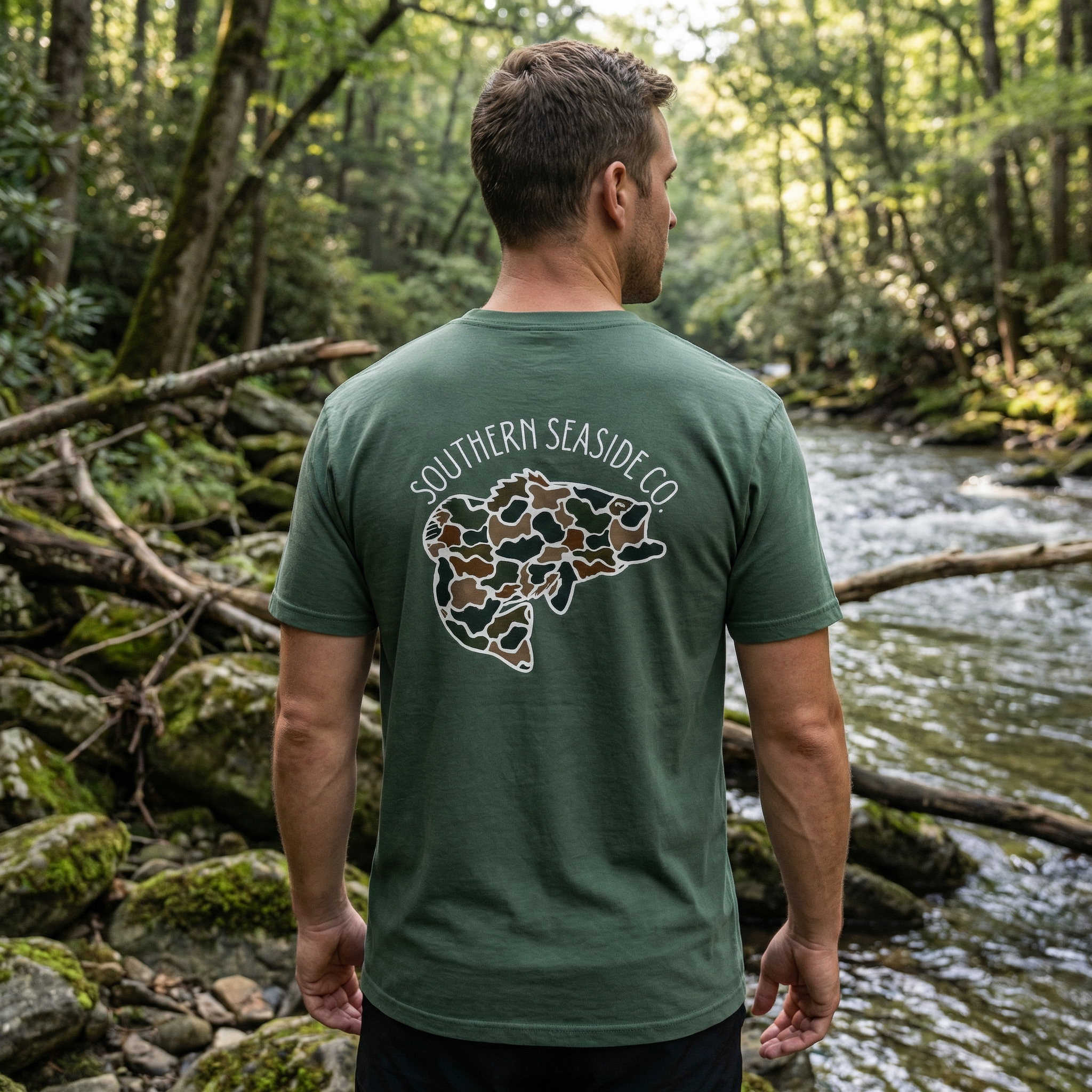 Man wearing a green bass fishing t-shirt in a camo print design with a logo in a forest setting 