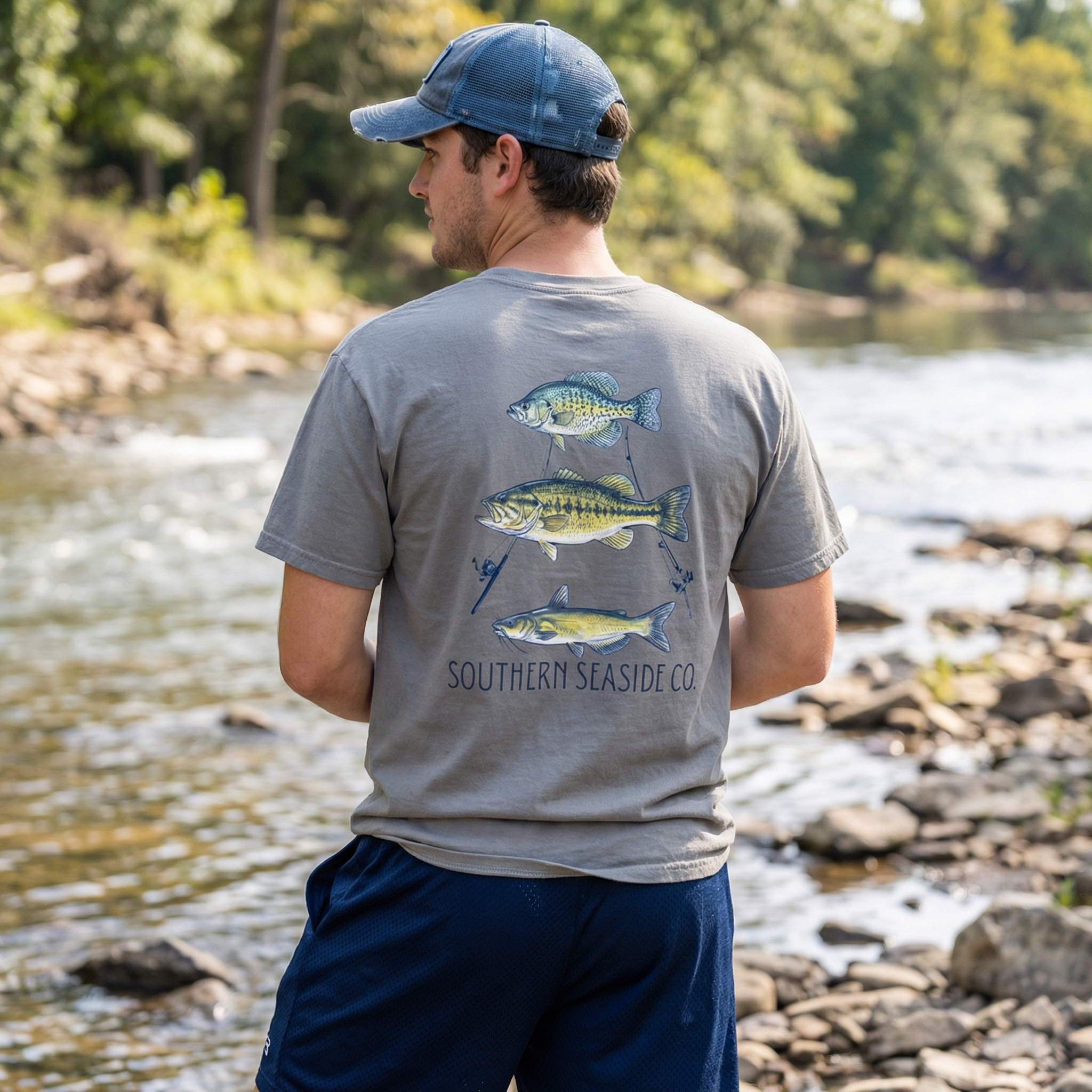 Men's freshwater fishing t-shirt. Man wearing a gray t-shirt with fish graphics by a river
