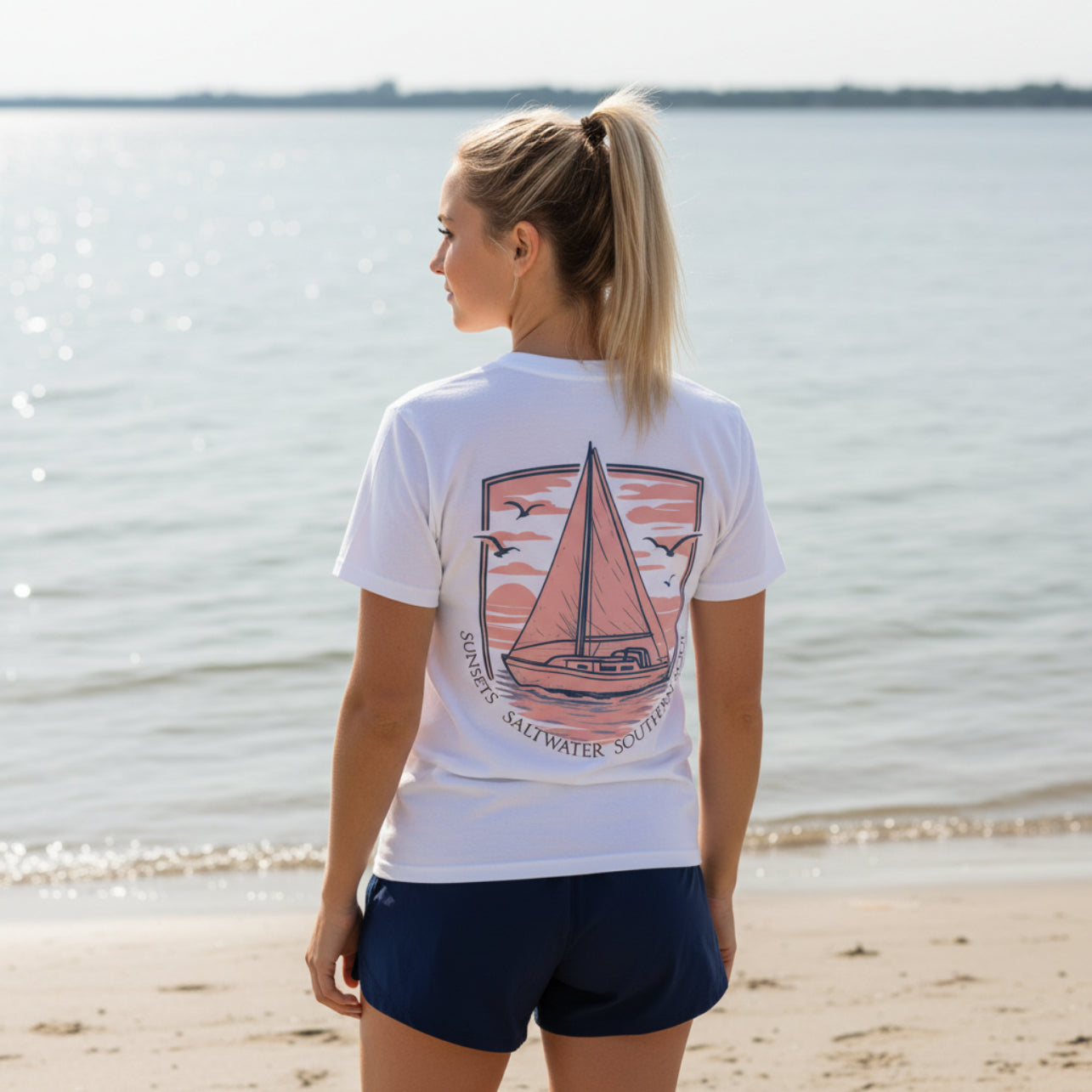 Woman wearing a white t-shirt with a sailboat design by the water