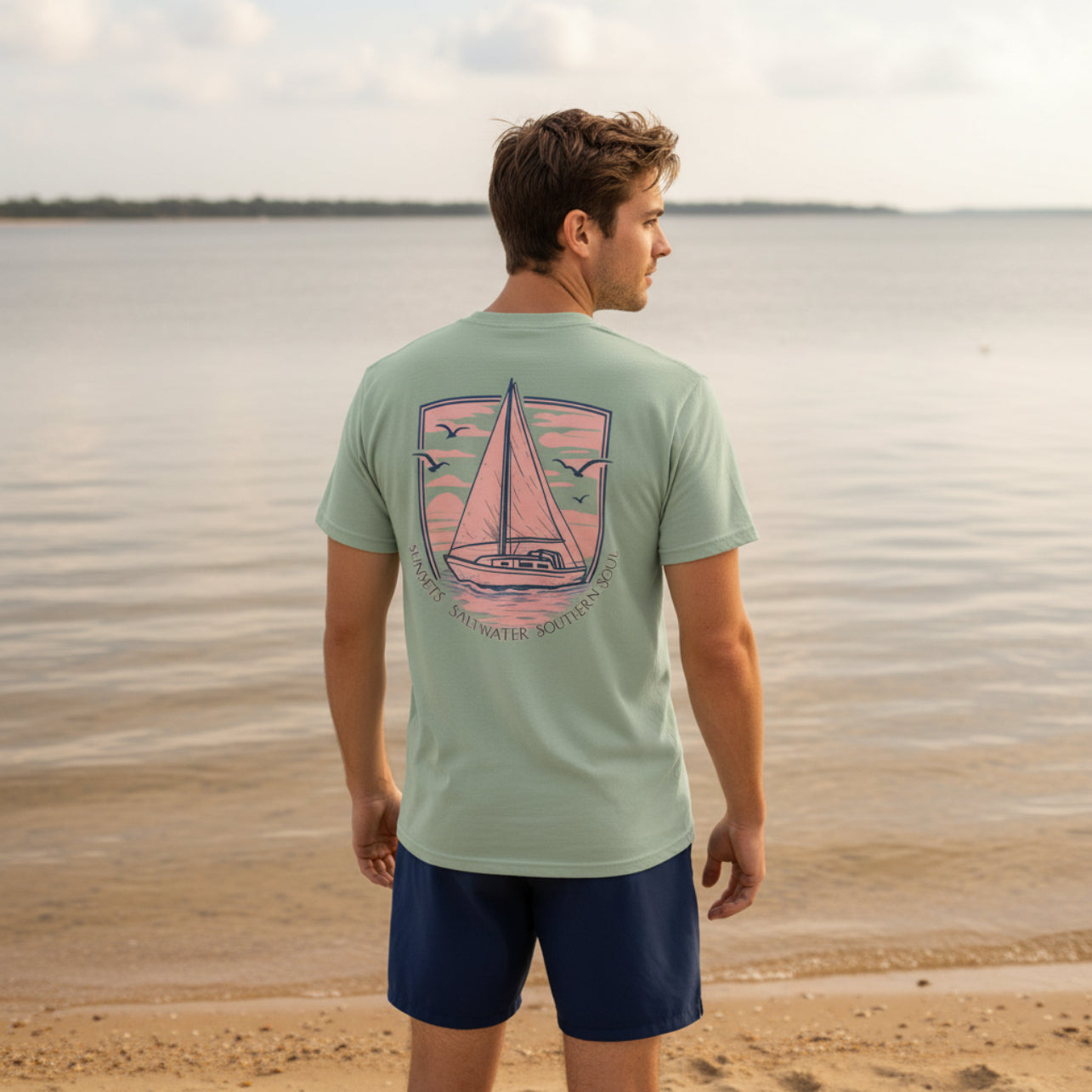 Man wearing a light green t-shirt with a sailboat design on a beach