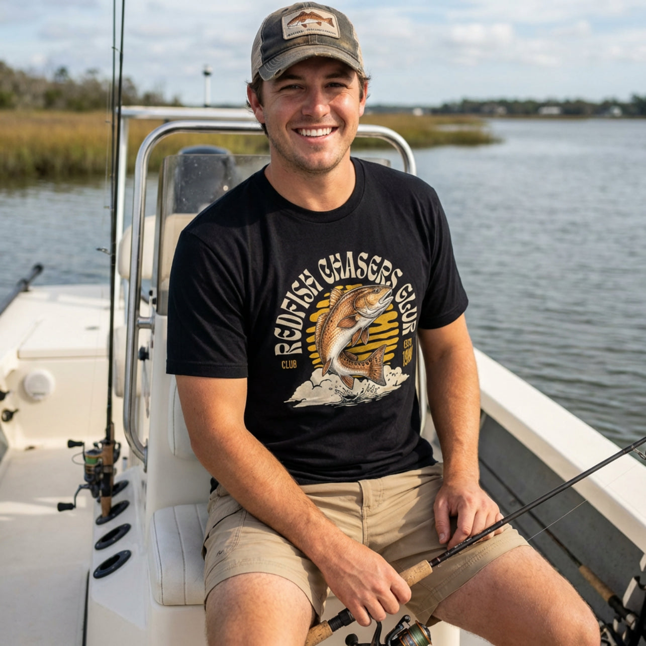 Man sitting on a boat wearing a black t-shirt with a redfish graphic t-shirt ].